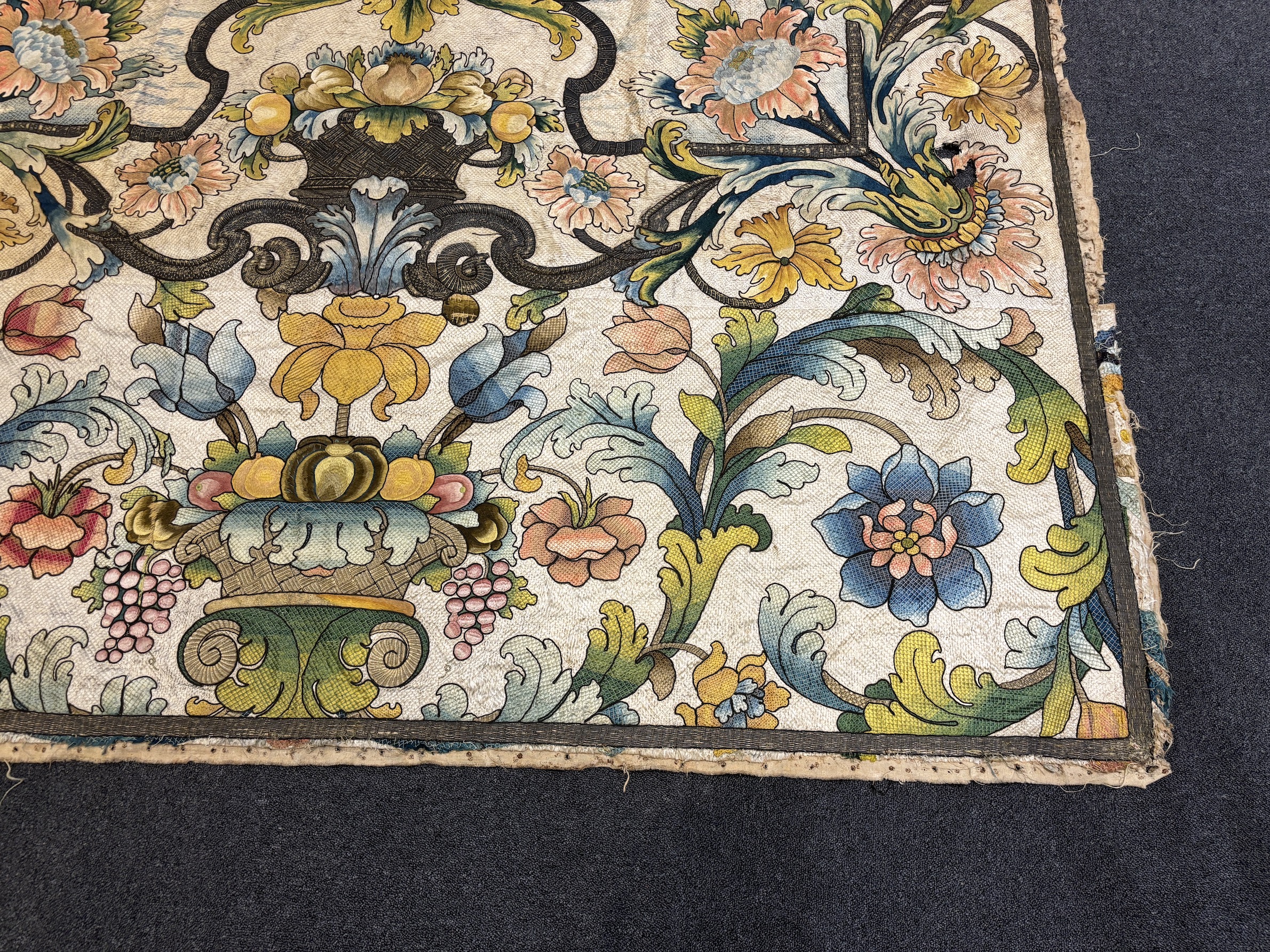 A large early 18th century possibly French polychrome and gold metallic silk embroidered wall hanging, with scrolling vine and floral border. The central motifs embroidered with an elaborate metallic thread cartouche fra